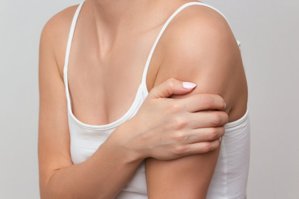 一个肩膀疼痛的女人，被隔离在一个明亮的背景下。女人的手托着疼痛的肩膀。图片下载