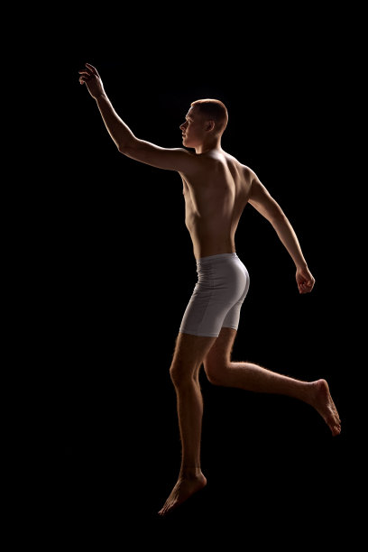 年轻有吸引力的红发男子穿着内衣的肖像，在黑暗的背景跳不寻常的姿势图片下载