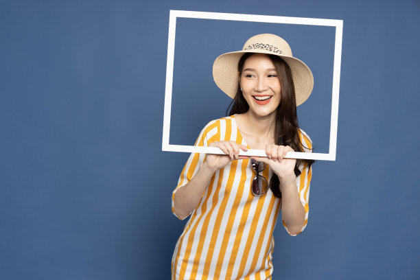 年轻的亚洲女游客拿着一个相框孤立的蓝色背景图片下载