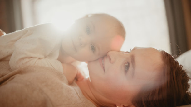 有爱心的年轻妈妈在家里玩和照顾可爱的宝宝。微笑的美丽妈妈和可爱的小婴儿在卧室拥抱。温柔时刻。图片下载