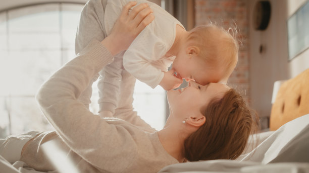 年轻有爱心的妈妈在家里玩和照顾可爱的宝宝。美丽的妈妈和可爱的小婴儿在卧室里拥抱。温柔时刻。图片下载