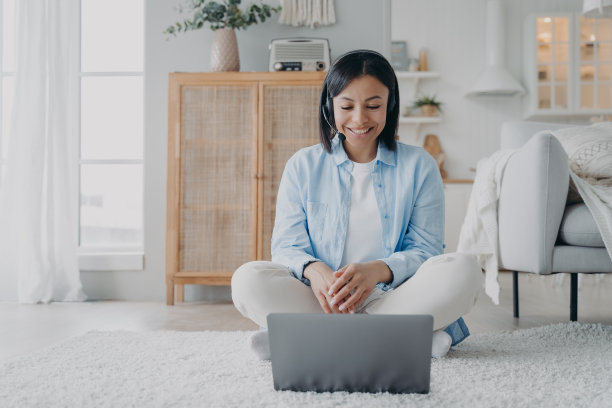 戴着耳机的女教练坐在地板上，用笔记本电脑进行视频通话，进行在线咨询图片下载