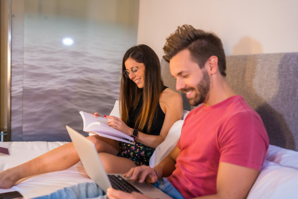 愉快的白人夫妇在酒店的床上用电脑和书图片下载