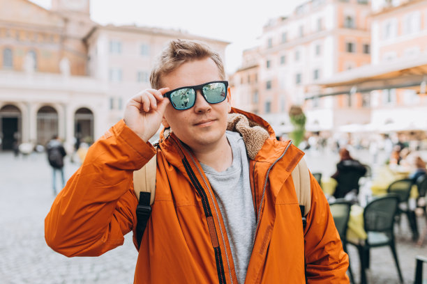 一个帅哥在城市里穿行的短镜头。戴着墨镜背着黄色背包的年轻人走在城市街道上图片下载