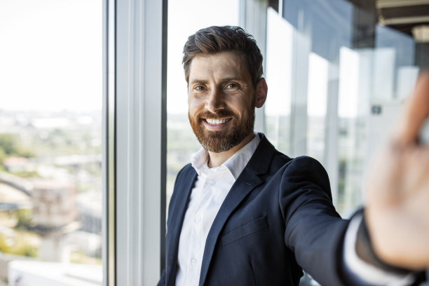 快乐的中年商人在办公室内部工作时进行视频通话或自拍，并对着镜头微笑图片下载