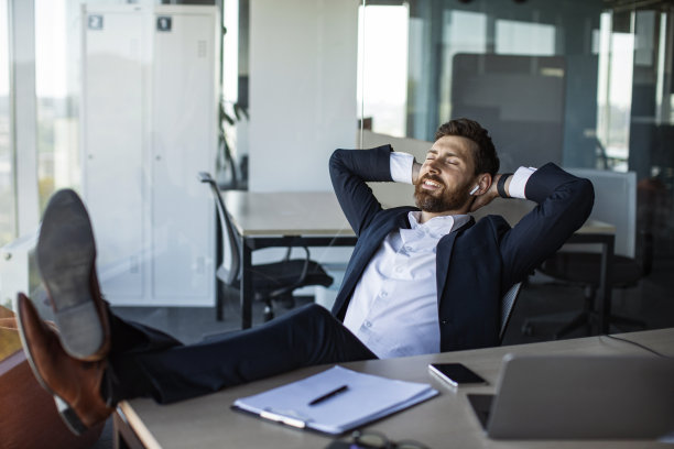 快乐放松的商人听音乐，靠在椅子上，腿放在桌子上，手放在脑后图片下载