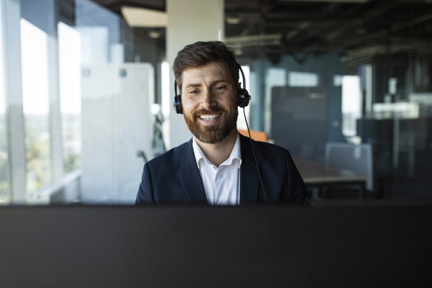积极的男性企业家，西装，戴着耳机，在办公室内部对着电脑摄像头讲话，自由空间图片下载