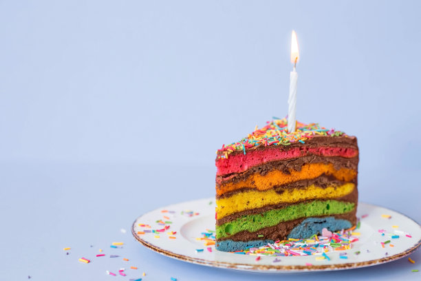 彩虹生日蛋糕装饰着喜庆的蜡烛和五彩纸屑。糖果。蓝色背景上彩虹的彩色甜点。图片下载
