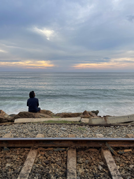 印度人坐在海岸线上的人造岩石海防上，海岸线(南部)铁路平行于海岸线，金属铁路轨道和砾石，海岸侵蚀抛石装甲墙，海岸管理，科伦坡，斯里兰卡图片下载