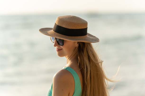 美丽的白人女子在绿松石比基尼沙滩帽和太阳镜漫步在海滩上享受海风和日落的景色图片下载