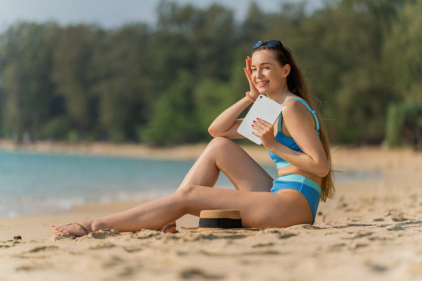 数字游牧民在海滩度假。美丽的白人女子在比基尼使用她的数字平板电脑与她的团队工作，并与她的朋友在海滩上愉快地交流图片下载