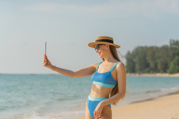 数字生活。穿着比基尼的美丽白人女子使用她的数字平板电脑与她的团队一起工作，并在海滩上与她的朋友愉快地交流图片下载