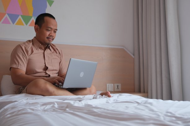 成年亚洲男人享受工作在他的床上与他的笔记本电脑图片下载