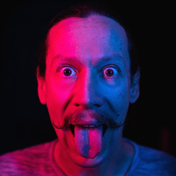 在蓝红色灯光下露出舌头的男人肖像图片下载
