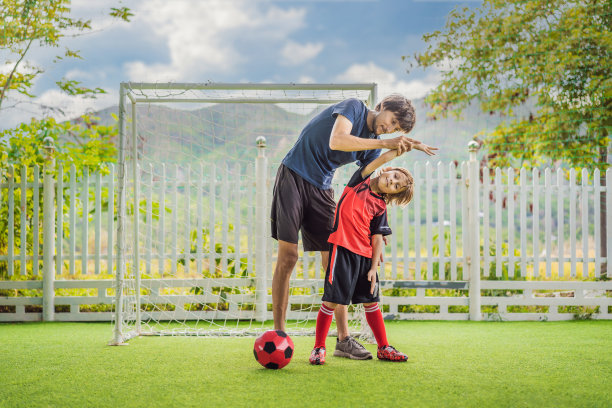 穿着红色足球服的小男孩和他的教练或父亲在户外做热身运动。活泼的孩子与孩子或父亲一起运动，微笑的快乐男孩在夏天玩得开心图片下载