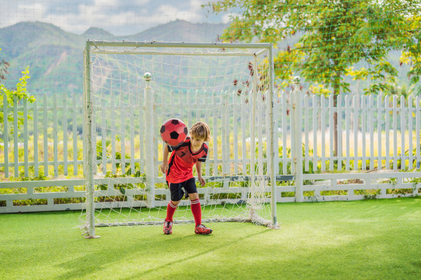 小男孩穿着红色的足球服踢足球，在户外踢足球。活泼的孩子与孩子或父亲一起运动，微笑的快乐男孩在夏天玩得开心图片下载