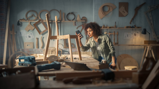 产品设计师正在用智能手机拍摄木椅项目照片。有创意的黑人女性在网上给同事发照片，寻求反馈和评价。图片下载