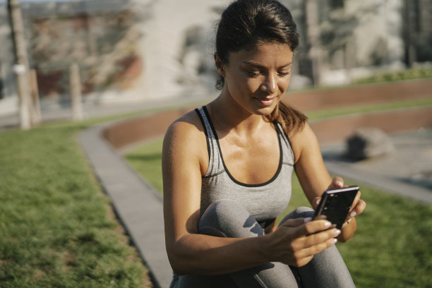穿着运动服的健美女子在外面打电话。图片下载