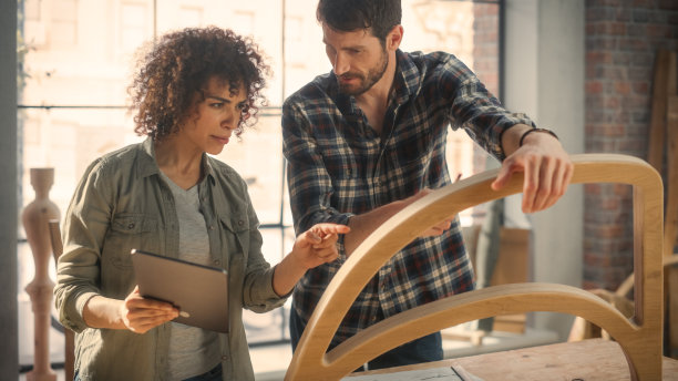 两个有才华的小企业主在家具车间使用平板电脑和讨论新木椅的设计。木匠和年轻的女学徒在阁楼工作室工作。图片下载