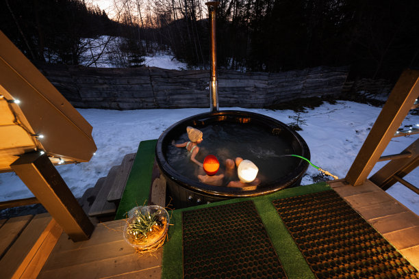 孩子们在小屋的露台上享受木桶热水浴缸的沐浴。带有壁炉的斯堪的纳维亚浴缸，可以燃烧木头和加热水。图片下载