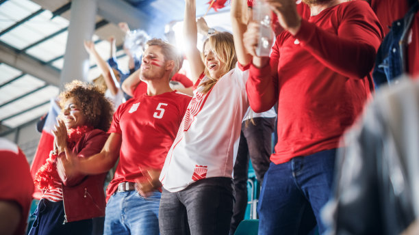 体育场大事件:一群球迷为红色足球队的胜利欢呼。人们庆祝进球，冠军。可爱的白种人夫妇涂了脸欢呼，欢呼。图片下载