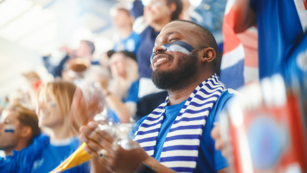 体育场馆大事件:英俊的黑人男子欢呼。一群脸上涂满彩绘的球迷为他们的蓝色足球队欢呼、呐喊。人们庆祝进球，冠军。图片下载