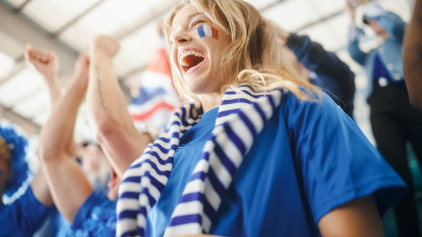 体育场足球赛:美丽的白人球迷女孩的肖像，脸上画着法国国旗，为她的球队加油。球迷欢呼，庆祝进球，冠军图片下载
