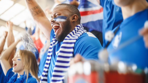 体育场馆大事件:英俊的黑人男子欢呼。一群脸上涂满彩绘的球迷为他们的蓝色足球队欢呼、呐喊。人们庆祝进球，冠军。图片下载