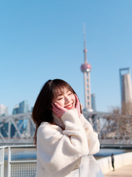 美丽的年轻女子，黑色长发，白色裙子摆出闭眼与上海外滩建筑背景在阳光灿烂的日子。情感、人、美、旅行、生活理念。图片下载