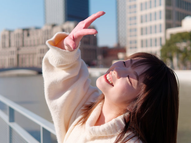 美丽的年轻女子，黑色长发，白色裙子摆出闭眼与上海外滩建筑背景在阳光灿烂的日子。情感、人、美、旅行、生活理念。图片下载