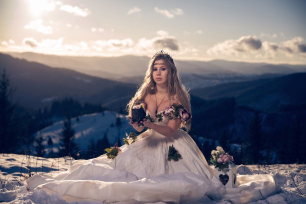 美丽的年轻女子穿着神秘的婚纱，上面有粉红色的花朵，在雪山上摆姿势图片下载