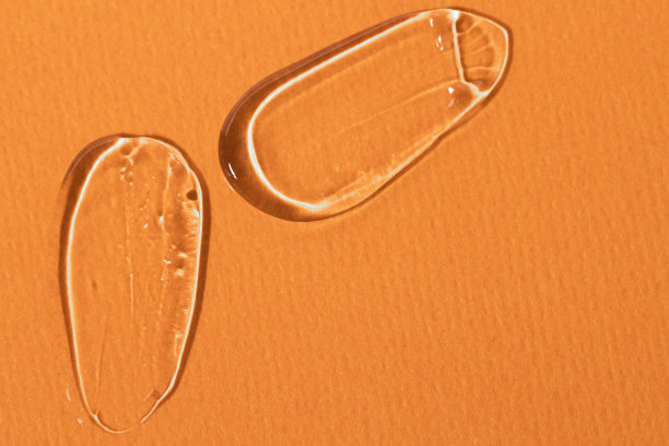 一些涂抹透明凝胶在橙色背景，俯视图。化妆品背景与液体纹理和复制空间。图片下载