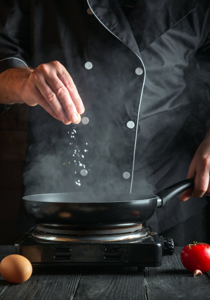 厨师在锅里煮鸡蛋时加盐。在老式厨房桌子上的工作环境。垂直的图像图片下载