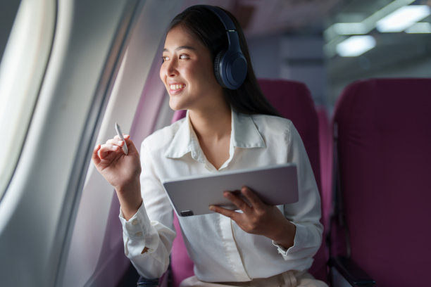 年轻迷人的亚洲商务女乘客坐在商务舱豪华飞机上，戴着无线耳机放松，在飞行中使用平板电脑工作图片下载