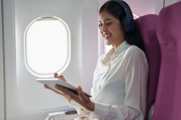 年轻迷人的亚洲商务女乘客坐在商务舱豪华飞机上，戴着无线耳机放松，在飞行中使用平板电脑工作图片下载