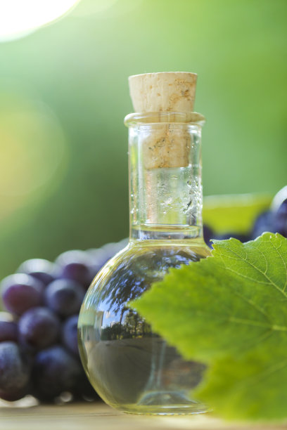 葡萄油在玻璃瓶里，葡萄串与绿叶在一个木锯切割在模糊的绿色花园背景。图片下载