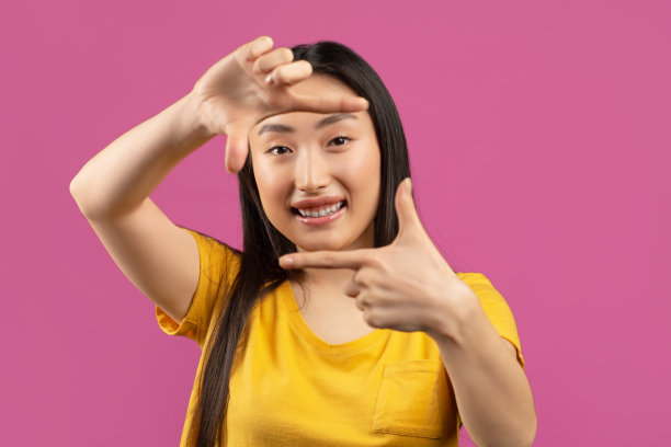 漂亮的亚洲女士通过手指像相机，在紫色背景上摆姿势，使照片相机框架图片下载