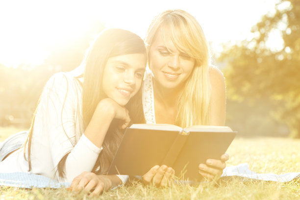 母女俩躺在阳光明媚的草地上看书图片下载