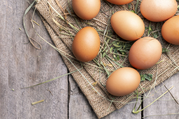 棕色的鸡蛋躺在干草和旧木板的背景上。图片下载