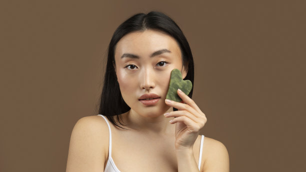 韩国女士按摩面部由刮刀石英石护肤，在棕色背景，全景图片下载