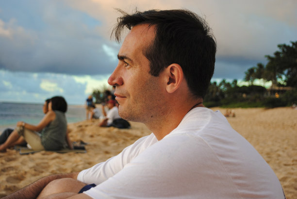 在美国夏威夷瓦胡岛的日落海滩上，一位年轻英俊的男子观看日落的侧视图图片下载