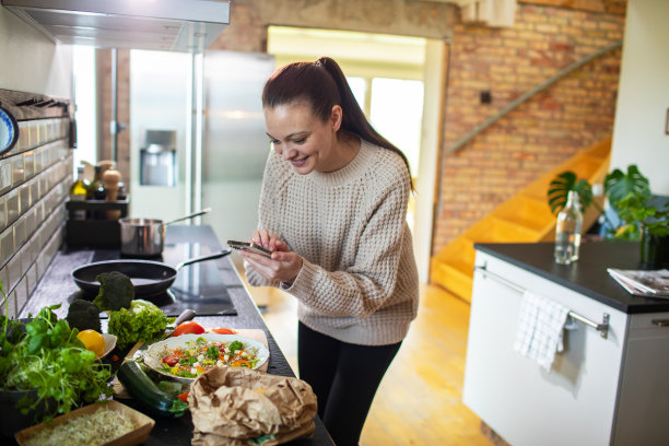一名年轻女子用智能手机拍下了她在家里厨房里做的沙拉图片下载