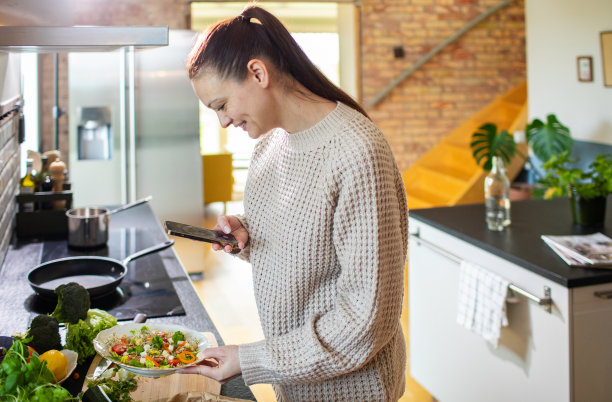 一名年轻女子用智能手机拍下了她在家里厨房里做的沙拉图片下载