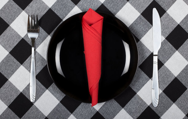 黑色的盘子，刀叉和红色的餐巾。盘子和餐具放在铺着格子布的桌子上图片下载