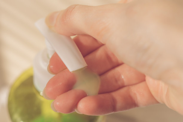 女性的手使用带有分配器的液体肥皂。绿色的凝胶滴在你的手掌。宏观照片图片下载