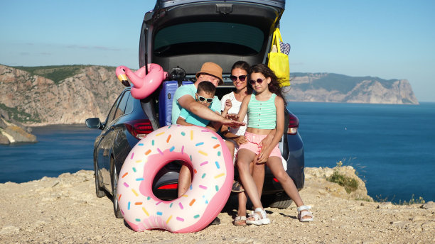 一个幸福的家庭坐在一辆汽车的后备箱里，笑着，看着大海。图片下载
