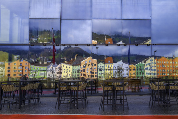 奥地利西部历史地标小镇蒂罗尔，因斯布鲁克的天际线上，充满活力的彩色房屋反射在玻璃窗上，人行道上空荡荡的长凳和桌子图片下载