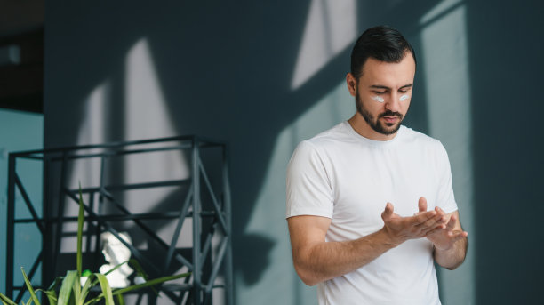 帅哥双手捧面霜，在脸上涂抹提升滋养抗皱霜。治疗软水皮肤。护肤概念图片下载