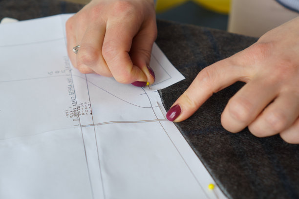 年轻的女裁缝把纸样钉在布料上。女裁缝用自己的双手缝制衣服图片下载