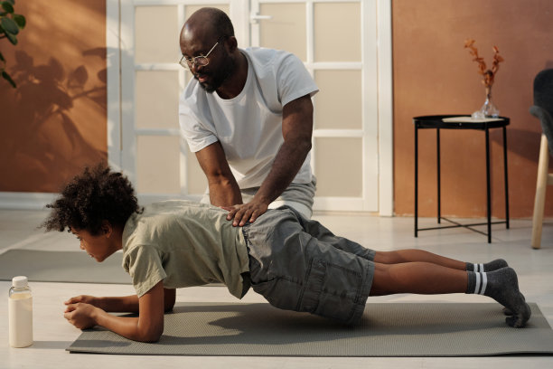 年轻的非裔美国人在运动服帮助他的儿子平板支撑图片下载